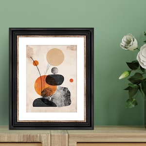 May include: A framed abstract print with a beige background and a stacked arrangement of black and gray rocks. The rocks are surrounded by orange and brown circles. The print is in a black frame.