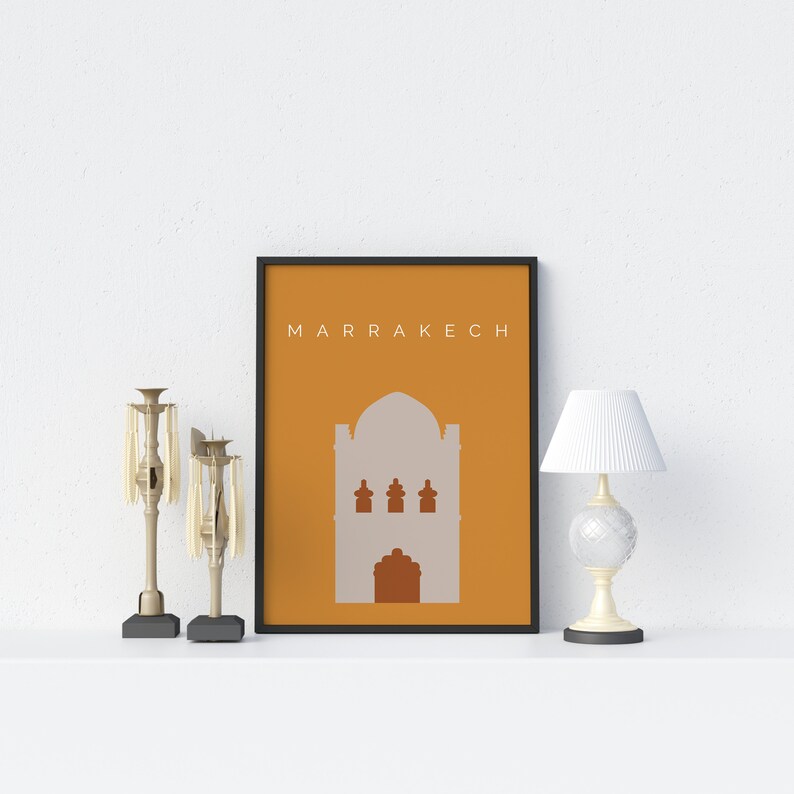 May include: A framed print with a minimalist illustration of a building in a warm orange color. The text "MARRAKECH" is printed in black at the top of the print.