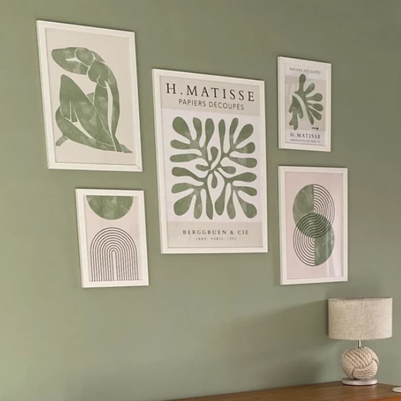 Op de afbeelding: Een wandgalerij met vijf ingelijste prints met abstracte ontwerpen in tinten groen en wit. De prints bevatten de tekst "H. Matisse Papiers Decoupes" en "Berggruen & Cie" samen met een gestileerd bladerontwerp en een geometrisch ontwerp.