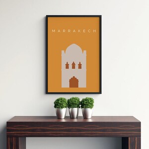 May include: A framed print with a minimalist design featuring a building silhouette in a light gray color against a yellow background. The text "MARRAKECH" is printed in white at the top of the print.