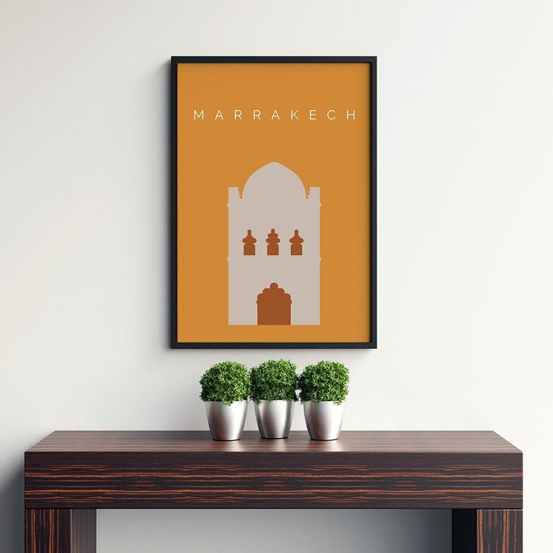 May include: A framed print with a minimalist design featuring a building silhouette in a light gray color against a yellow background. The text "MARRAKECH" is printed in white at the top of the print.