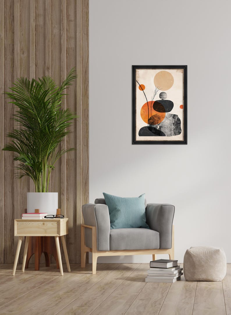 May include: Abstract art print in a black frame. The artwork features orange, black, and gray shapes on a beige background. The print hangs above a gray armchair with a blue pillow. A potted plant and side table are also in the room.