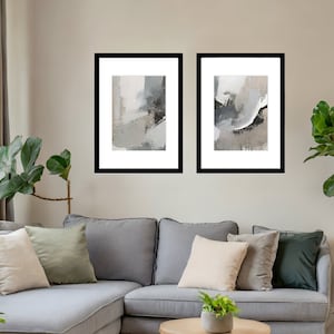 May include: Two framed abstract art prints with black frames and white mounts. The prints feature grey and white abstract shapes with black accents.