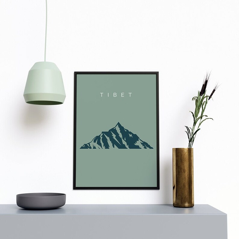 以下が含まれることがあります： 薄い緑色の背景に濃い青色の山のシルエットが描かれた、ミニマルなデザインの額装されたプリント。プリントの上部には白い文字で「TIBET」と印刷されています。