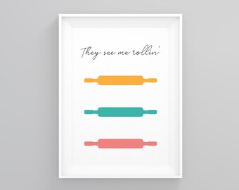 May include: A white framed print with the text "They see me rollin'" in black cursive font. Three rolling pins are shown in the center of the print, one yellow, one teal, and one pink.