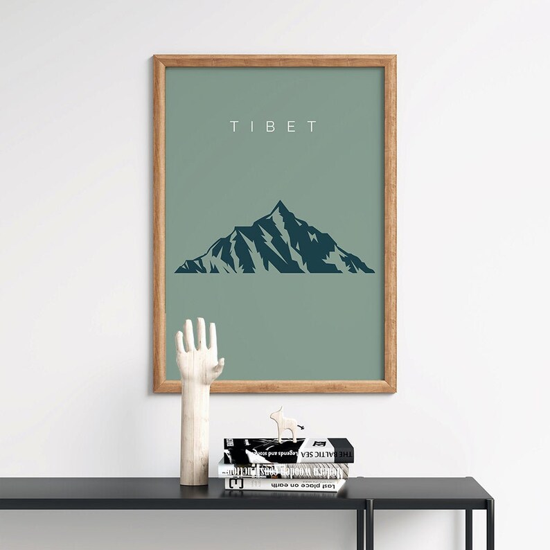 以下が含まれることがあります： 緑色の背景と濃い青色の山のシルエットが描かれた額装されたプリント。プリントの上部には白い文字で「TIBET」と印刷されています。