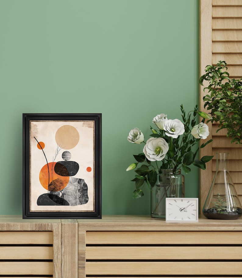 May include: A black framed print with an abstract design of stacked stones and circles in orange, brown, and black against a beige background.
