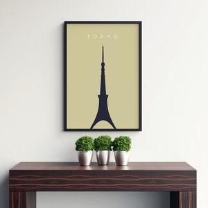 May include: A black framed print with a beige background and a black silhouette of the Tokyo Skytree. The text "TOKYO" is printed in white at the top of the print. The print is hanging on a white wall above a dark wood table with three green potted plants.