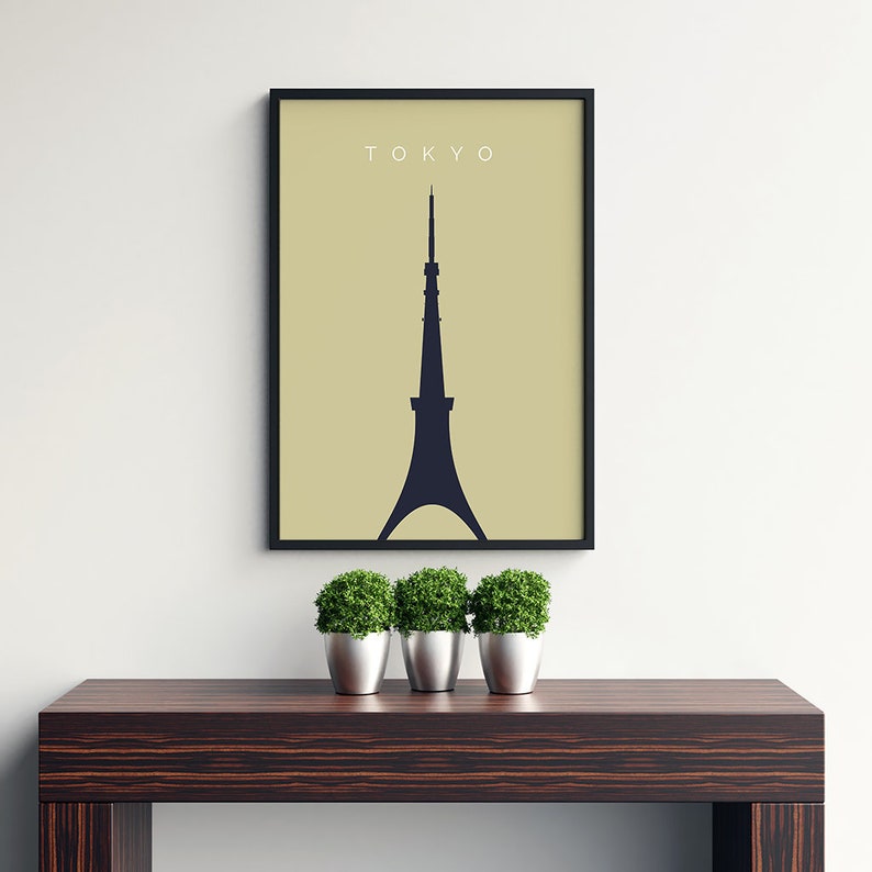 May include: A black framed print with a beige background and a black silhouette of the Tokyo Skytree. The text "TOKYO" is printed in white at the top of the print. The print is hanging on a white wall above a dark wood table with three green potted plants.
