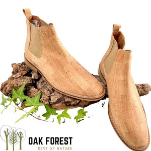 Puede incluir: Un par de botines de corcho con un dise&ntilde;o de f&aacute;cil calce. Las botas son de color marr&oacute;n claro y tienen una superficie de corcho texturizada. Las botas est&aacute;n sobre un trozo de corteza de &aacute;rbol con hojas verdes.