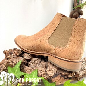 Puede incluir: Botas de tobillo de corcho con un panel el&aacute;stico marr&oacute;n en la parte posterior. Las botas est&aacute;n sobre un trozo de corteza de &aacute;rbol con hojas verdes. El texto "OAK FOREST BEST OF NATURE" es visible en la parte inferior de la imagen.