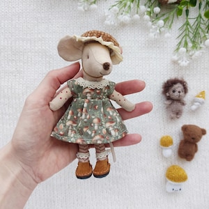 Könnte beinhalten: Eine handgefertigte Mauspuppe mit einem grünen Kleid mit Pilzmuster, einem braunen Hut und Stiefeln. Zusätzliche Miniatur-Filzfiguren von Pilzen und Tieren sind ebenfalls vorhanden.