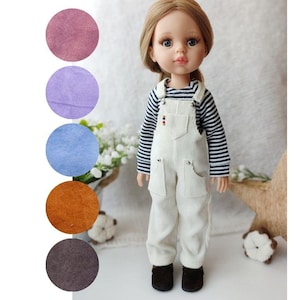 Puede incluir: Una muñeca con un mono de pana blanco y una camisa a rayas azules y blancas. La muñeca tiene el pelo largo y rubio y los ojos azules.