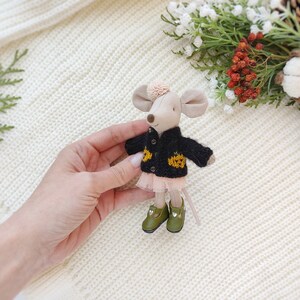 Puede incluir: Un peque&ntilde;o rat&oacute;n de peluche que lleva un c&aacute;rdigan de punto negro con detalles de calabaza amarilla y una falda de tul rosa. El rat&oacute;n tiene zapatos verdes y un lazo rosa en la cabeza.