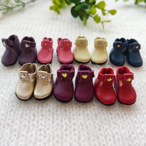 Peut inclure: Dix paires de chaussures en cuir miniatures de différentes couleurs, dont le violet, le rose, l'or, le bleu et le rouge. Chaque chaussure a un petit accent doré.