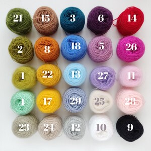 Puede incluir: Una colecci&oacute;n de 29 ovillos de lana de varios colores, numerados del 1 al 29. La lana est&aacute; dispuesta en cinco filas de seis ovillos cada una, con un ovillo en la fila inferior.