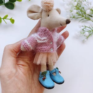 May include: A small, handmade mouse doll wearing a pink and white striped sweater, a tulle skirt, and blue shoes with berry accents.