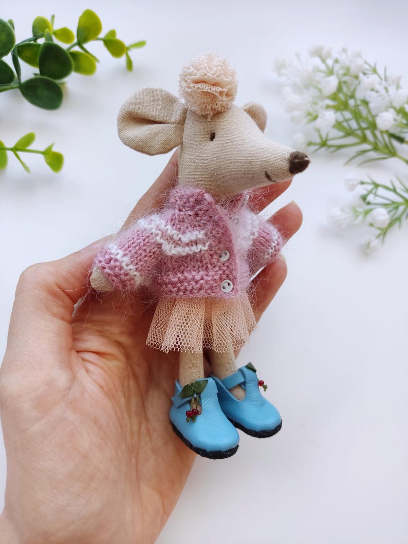 May include: A small, handmade mouse doll wearing a pink and white striped sweater, a tulle skirt, and blue shoes with berry accents.