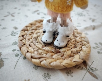 May include: A small doll wearing a yellow sweater, pink skirt, and white boots with black eyes. The doll is standing on a woven straw mat.