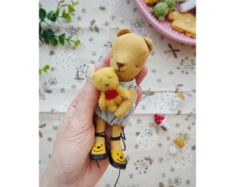 May include: A yellow teddy bear wearing a blue and white outfit and yellow shoes with a smiley face design is holding a smaller yellow teddy bear.