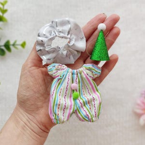 May include: A colourful striped onesie with a white ruffle headband and a green glitter party hat. The outfit is perfect for a baby or toddler.