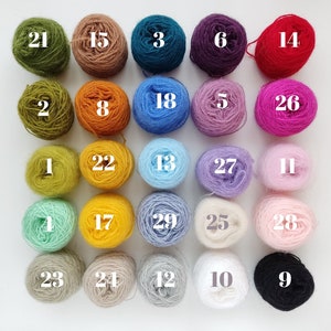 Op de afbeelding: Een verzameling van 29 bollen garen in verschillende kleuren, genummerd van 1 tot en met 29. Het garen is gerangschikt in vijf rijen van zes bollen, met &eacute;&eacute;n bol in de onderste rij.