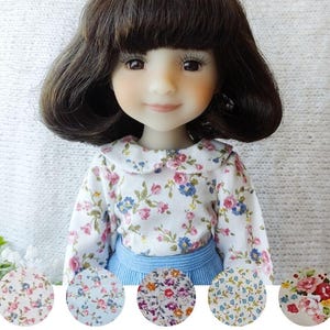 May include: A doll with brown hair wearing a white blouse with a floral pattern of pink, blue, and purple flowers. The doll is also wearing a blue skirt. Five fabric swatches with floral patterns are shown below the doll.