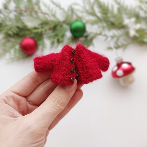 Op de afbeelding: Een klein rood gebreid vestje met bruine knopen.