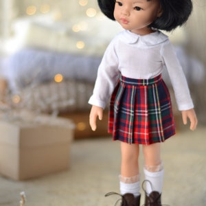 May include: A doll with black hair wearing a white collared shirt and a red and black plaid skirt. The doll is wearing brown shoes and white socks. The doll is standing on a wooden platform.