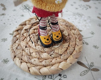 May include: A small doll with red and white striped stockings and yellow shoes with a smiley face design. The doll is standing on a round woven straw mat.