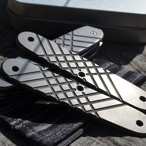 May include: Two grey metal knife handles with a diamond pattern. The handles are made of a textured metal and have a brushed finish.