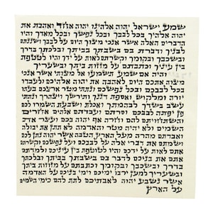 May include: A rectangular, off-white paper with black Hebrew text. The text is densely packed, filling the entire surface. The script appears to be a religious passage, likely a prayer or a sacred text.