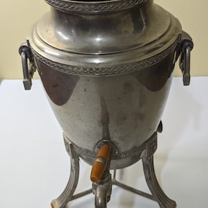 May include: A silver-colored metal coffee pot with a wooden handle and a three-legged base.