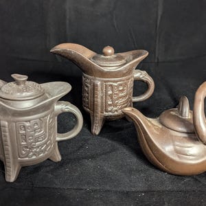May include: Three brown ceramic teapots with lids. One teapot is shaped like a swan, another is a traditional Chinese design, and the third is a more modern design.