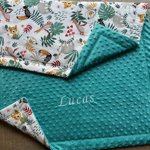 May include: A teal baby blanket with a white and colorful jungle animal print. The blanket features a soft, textured surface and the name "Lucas" embroidered in white.