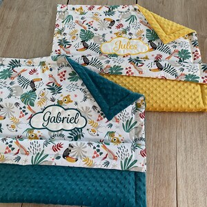 Peut inclure: Deux couvertures pour b&eacute;b&eacute; personnalis&eacute;es avec un imprim&eacute; d'animaux de la jungle. La couverture du haut est jaune avec le nom "Jules" brod&eacute; dessus. La couverture du bas est verte avec le nom "Gabriel" brod&eacute; dessus.