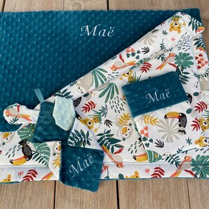 May include: A teal baby blanket and matching accessories with a jungle-themed pattern featuring toucans, sloths, and monkeys. The blanket and accessories are embroidered with the name "Ma&euml;". The blanket has a textured surface.