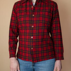 Puede incluir: Una camisa de manga larga con botones de cuadros rojos, azules y amarillos. La camisa tiene cuello y un corte holgado.