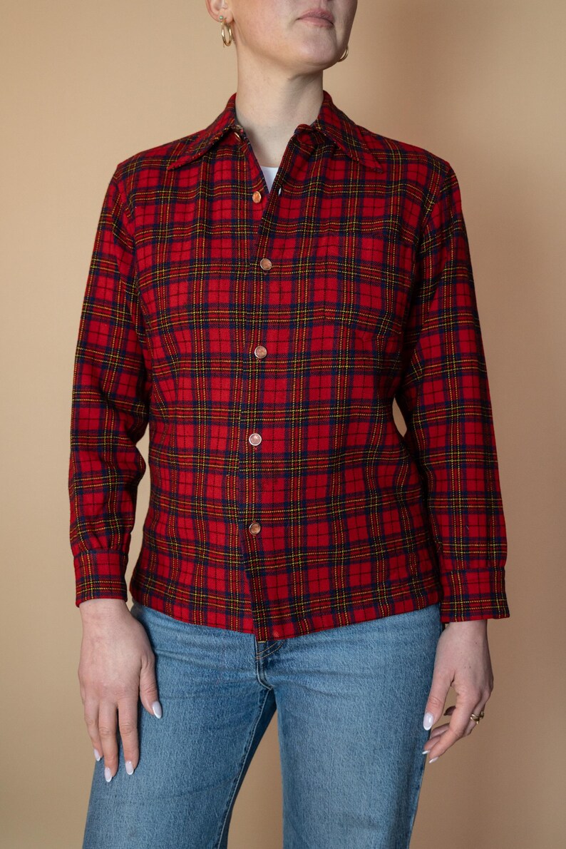 Puede incluir: Una camisa de manga larga con botones de cuadros rojos, azules y amarillos. La camisa tiene cuello y un corte holgado.