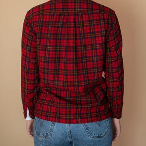 Puede incluir: Una camisa de franela a cuadros rojos y negros con mangas largas y cuello abotonado. La camisa se lleva sobre un par de pantalones vaqueros azules.