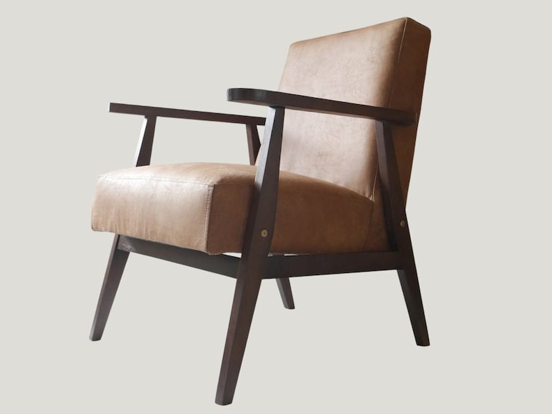 K&ouml;nnte beinhalten: Ein brauner Ledersessel mit einem dunklen Holzrahmen und abgewinkelten Beinen. Der Sessel hat ein schlichtes, modernes Design aus der Mitte des Jahrhunderts.