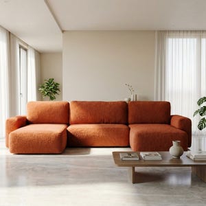 Może przedstawiać: Nowoczesna, modułowa pomarańczowa sofa z pasującą otomaną, ustawiona w jasnym, przestronnym salonie. Sofa połączona jest z niskim, prostokątnym drewnianym stolikiem kawowym. Pokój posiada duże okna, przezroczyste zasłony i rośliny doniczkowe.
