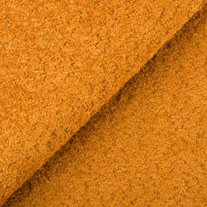 Op de afbeelding: Close-up van gevouwen, getextureerde stof in een warme, goudoranje tint. Het materiaal heeft een dichte, noppenachtige oppervlakte, wat wijst op een pluche of getextureerde textiel. De plooien van de stof cre&euml;ren schaduwen en diepte.