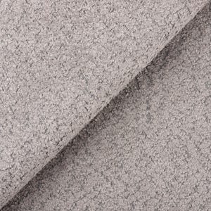 Op de afbeelding: Close-up van een lichtgrijze stof met een getextureerd, noppig oppervlak. De stof is gevouwen en onthult een diagonale vouw. Het materiaal lijkt zacht en kan worden gebruikt voor bekleding of kleding.