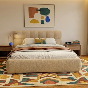 Könnte beinhalten: Ein beige gepolstertes Bett mit passendem Kopfteil und Fußteil. Das Bett ist mit weißer Bettwäsche, einer gestreiften Decke und dekorativen Kissen ausgestattet. Ein farbenfroher geometrischer Teppich liegt am Fuß des Bettes. Ein abstraktes Kunstwerk hängt über dem Bett.