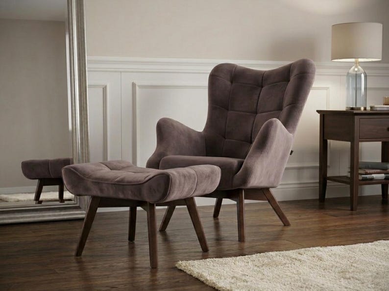 May include: A taupe-coloured wingback armchair and matching ottoman featuring a tufted backrest and seat cushion. Both pieces are supported by four dark brown wooden legs angled outward, providing a stable base for the upholstered furniture set.