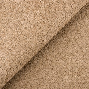Op de afbeelding: Close-up van een getextureerde stof in een warme, neutrale beige kleur. Het materiaal heeft een noppige, licht onregelmatige oppervlakte, met een gevouwen gedeelte dat een diagonale lijn cre&euml;ert. De stof ziet er zacht en uitnodigend uit.