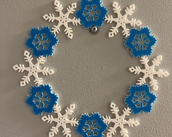 May include: A white and blue snowflake wreath with a silver screw in the center. The wreath is made of paper snowflakes and is a festive decoration for the winter holidays.