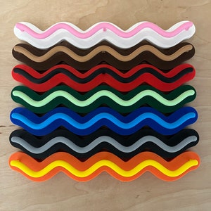May include: A collection of colorful, wavy-shaped objects. The colors include white, pink, brown, dark brown, red, green, blue, black, orange, and yellow. Each object has a unique color combination, creating a vibrant and eye-catching display. The objects are arranged in parallel rows.