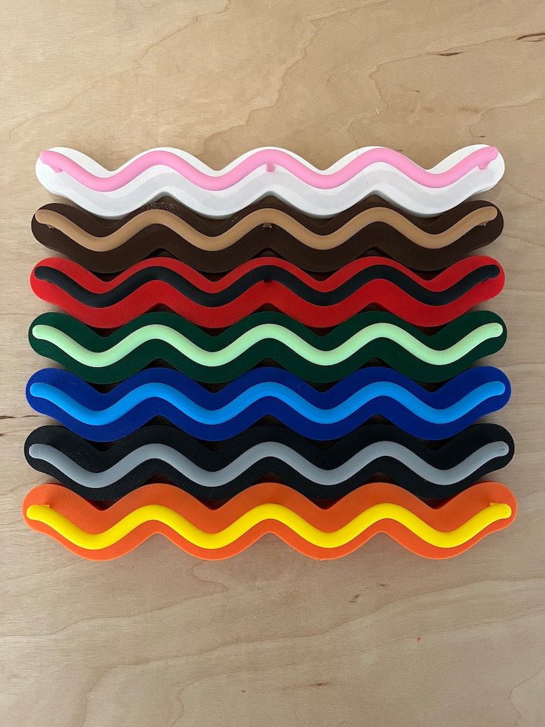 May include: A collection of colorful, wavy-shaped objects. The colors include white, pink, brown, dark brown, red, green, blue, black, orange, and yellow. Each object has a unique color combination, creating a vibrant and eye-catching display. The objects are arranged in parallel rows.